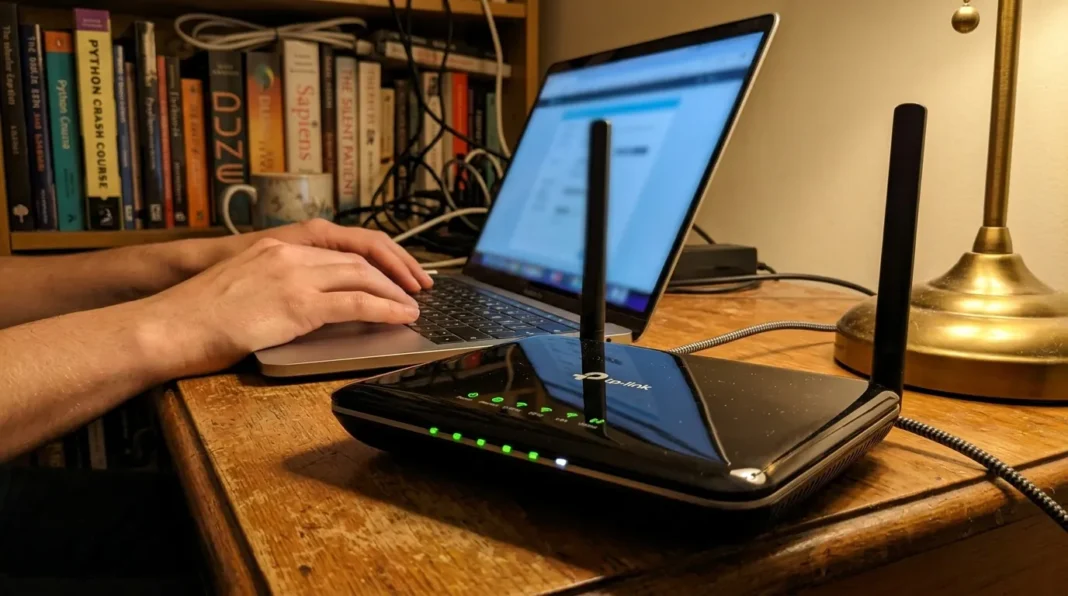 Espace de travail avec routeur WiFi Main sur clavier laptop, routeur WiFi noir sur bureau